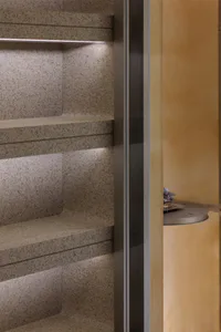 Close-up of built-in terrazzo niche shelves with warm integrated LED strip lighting and a glimpse of a round side table in the background.