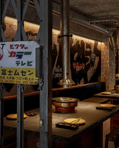Interior view of a Japanese yakiniku restaurant featuring a dark granite counter, built-in copper hot pot, stainless steel ventilation hood, concrete walls with graffiti-style murals, and Japanese signage.