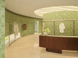Modern clothing boutique interior featuring curved walls covered in light green ceramic tiles, a curved wooden service counter, clothing racks, and a skylight ceiling.