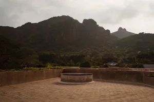 Rooftop terrace with circular concrete feature, brick pavers, and expansive view of forested mountains at dusk