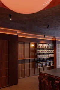 Interior view of a modern coffee shop featuring dark terrazzo walls, wooden shelving displaying coffee bags, and a large glowing pink spherical pendant light dominating the ceiling.