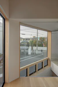 室內轉角設有淺橡木嵌入式窗邊座椅和大角度景觀窗，俯瞰日本街道，可見行人和電線桿。