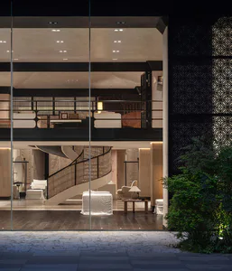 Exterior night view through large glass walls into a modern luxury double-height living room with a curved spiral staircase, white upholstered furniture, dark wood floors, and a patterned decorative screen on the right.