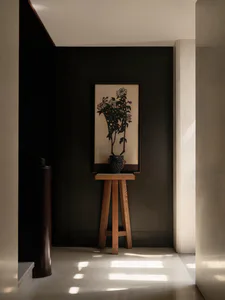Modern dark entryway with light oak three-legged console table, dark ceramic vase, and large framed black chrysanthemum silhouette artwork on a dark wall.