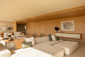 Modern minimalist living room with a large cream-colored ribbed sectional sofa, oak wood panel walls, built-in console, and colorful abstract painting.