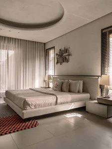 Modern minimalist bedroom featuring a curved concrete-like ceiling, textured plaster walls, a low platform bed with woven headboard, neutral bedding, two geometric table lamps, and colorful checkered and striped rugs.