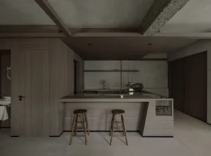 Modern minimalist kitchen with a large wooden island, two wooden stools, concrete walls and ceiling beams, and a built-in espresso machine.