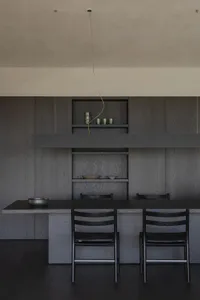 Modern minimalist dining room featuring dark wood cabinetry, floating open shelves, a long black dining table, and matching dark wood chairs under a single pendant light.