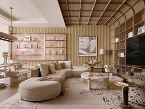Modern luxury living room with a large beige curved sectional sofa, travertine coffee table, built-in arched bookshelves, and textured beige walls under a coffered ceiling.