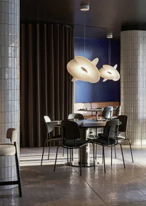 Modern restaurant interior featuring a round dining table with dark upholstered chairs, large sculptural white pendant lights, cylindrical tiled columns, a dark pleated curtain, and a blue accent wall in the background.