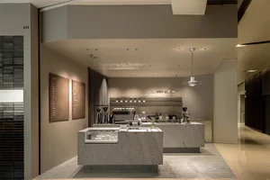 Modern minimalist coffee shop interior with grey terrazzo counter, pendant light, menu boards, and professional espresso equipment.