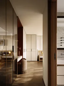 現代奢華更衣區，胡桃木飾面、米白色嵌入式衣櫃、兩張帶流蘇的圖紋梳妝椅，以及透過開放門道可見的大理石浴室。