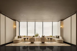 Modern minimalist living room with a large curved cream sofa, two patterned velvet swivel chairs, dark reflective floor, and large windows with sheer blinds.