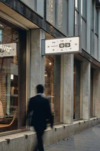 現代精品店店面，搭配大面積大理石柱與面板，懸掛著簡約白色時鐘招牌顯示 OB 於 Pitt Street 62 號，一位行人以動態模糊經過。