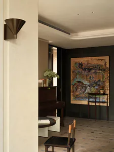 Modern entryway featuring a dark wood upright piano, a large abstract painting, a wooden chair, and a potted plant under warm lighting.