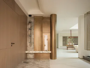 Modern entryway featuring a curved brass feature wall, marble console, cylindrical column, and integrated lighting, leading to a bright open-plan living area.