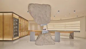 現代奢華零售空間內部，一塊巨大的懸浮巨石雕塑置於原石基座上的礦物展示櫃上方，背景為曲線木質櫃檯與燈光展示櫃。
