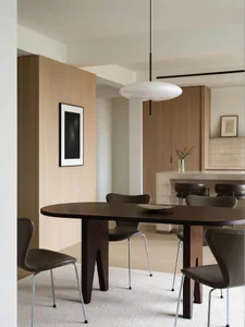 Modern minimalist dining room featuring a dark walnut oval table with sculptural legs, surrounded by brown leather chairs with metal bases, under a large white disc pendant lamp.