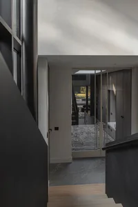 Modern interior view from a staircase landing looking down into a contemporary entryway with dark marble tile floors, a glass railing, built-in cabinetry, and a view into a bright living room with outdoor access.