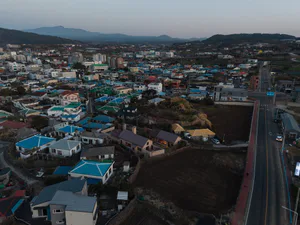 Aerial photograph of a densely built Taiwanese residential town at dusk, featuring colorful rooftops, agricultural fields, a main road, and distant mountains.