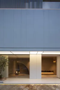 Modern minimalist building entrance featuring large limestone panels, recessed lighting, a curved glass wall with a metallic sphere sculpture, and warm interior wood tones.
