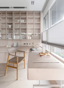 Modern minimalist home office with light wood built-in cabinetry, a wooden chair with upholstered seat, large windows with blinds, and decorative objects on the desk.
