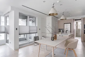 Modern minimalist dining room and kitchen with white walls, light wood flooring, a large dining table with wire-frame and upholstered chairs, and two white pendant lights hanging over the island.