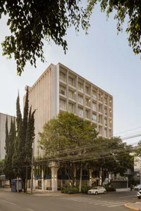 Exterior view of a multi-story brutalist concrete residential building with vertical columns and balconies, surrounded by lush trees and overhead power lines at street level.