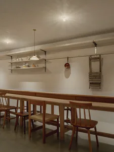 長型木製共享餐桌搭配橡木椅，漂浮層板上擺放餐具，懸掛銅鍋與木梯靠在白色磁磚牆上。