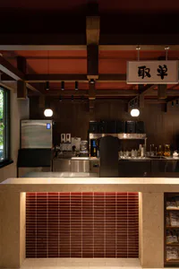 日式咖啡店服務吧台內部視角，包含深色木質壁板、淺色水磨石檯面、紅色磁磚基座與懸掛的球形吊燈。
