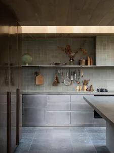Modern minimalist kitchen featuring concrete cabinetry, grey tiled walls, open shelving with hanging utensils, a concrete island, and warm wood ceilings.
