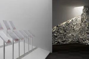 Modern art gallery interior featuring a large wall covered in crumpled reflective silver foil next to a row of white acrylic sign stands on a white platform.