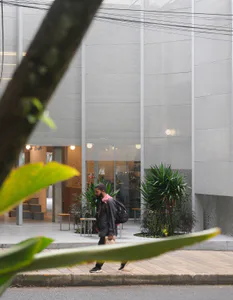 現代清水模咖啡店立面，大片玻璃窗、熱帶植物，以及走在台北人行道上的男子。
