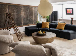 Modern living room with a large black sectional sofa, round wooden coffee table, beige linen armchairs, antique Japanese byobu screen, and large paper lantern pendant light.