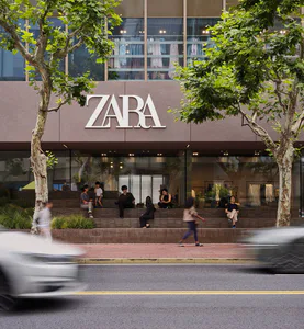 ZARA現代店面的街景，大面積玻璃櫥窗、質感石材立面，民眾坐在寬闊階梯上，背景有茂密的法國梧桐。