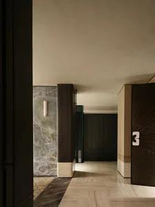 Modern luxury apartment hallway featuring green marble wall with vertical light fixture, dark wood paneling, light wood herringbone floor, and an elevator door marked with the number 3.