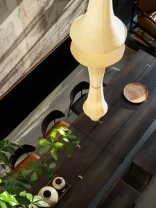 High-angle view of a modern dining room with a dark walnut wood table, black and brown leather chairs, a large sculptural paper pendant lamp, and a potted plant in the foreground.