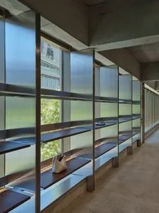 Modern brutalist entryway featuring concrete walls, steel-framed frosted glass panels, and dark walnut floating shelves used for shoe and bag storage.