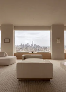 Modern minimalist living room with a large boucle fabric daybed and chaise in the foreground, overlooking the New York City skyline including One World Trade Center through a floor-to-ceiling window.