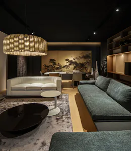 Modern luxury living and dining area featuring a large woven rattan pendant light, white leather sofa, dark teal sectional, black oval coffee table, and traditional Chinese ink painting on the back wall.