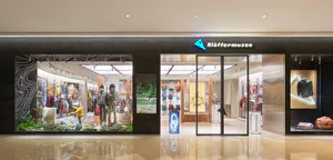 Modern retail storefront of Klattermusen outdoor brand in Taipei, featuring a dramatic black facade, large glass windows with nature-themed displays including rocks, moss, mannequins in outdoor gear, and white topographic line illustrations.