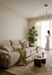 Bright and airy living room featuring a large off-white sectional sofa, marble nesting coffee tables, a dramatic crystal chandelier, and a tall fiddle-leaf fig plant by the arched window.