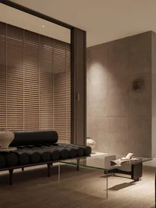Modern minimalist living room featuring a black leather cylindrical daybed, glass coffee table, textured concrete walls, and wooden blinds with warm ambient lighting.