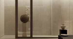 Modern minimalist entryway featuring large travertine stone tiles, a sculptural sphere made of twigs on a stone pedestal, a ceramic vase on a black plinth, and a dark leather bench.