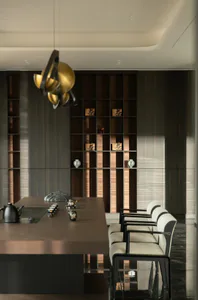 Modern minimalist dining and tea room featuring a long walnut table, sculptural gold and black chandelier, built-in dark wood display shelves with tea artifacts, and four white upholstered armchairs.