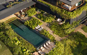 Aerial photograph of a modern rooftop terrace with a rectangular infinity pool, wooden decking, multiple lounge areas, and dense tropical vegetation on a contemporary dark building.