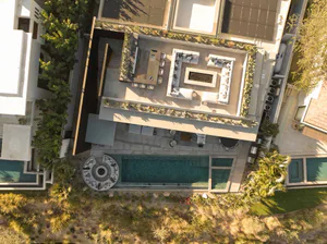 Bird's eye view of a modern luxury villa rooftop terrace with a rectangular swimming pool, circular conversation pit, large U-shaped outdoor sofas, dining area, and extensive concrete decking surrounded by desert landscaping.