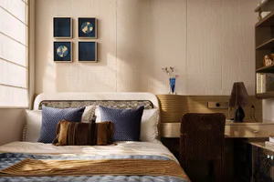 Modern neutral-toned bedroom with a bed dressed in white and blue bedding, multiple blue and brown decorative pillows, a mosaic headboard, textured beige wall panels, four pieces of blue wall art, a wooden desk with a woven brown chair, and a blue glass vase with flowers.