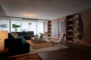 Modern living room featuring dark green sectional sofa, geometric wood paneling in warm tones, built-in bookshelves, a white shearling and leather sling chair, and a large patterned area rug under a low wooden coffee table.