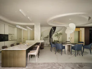 Modern luxury open-plan kitchen and dining area featuring a large round marble dining table with blue upholstered chairs, a long marble kitchen island with pendant lights, and a striking black and white spiral staircase in the background.